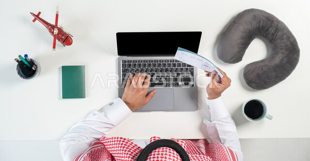 Buying airline tickets online, using websites to search for flights, a close-up portrait of a Saudi Gulf Arab man using a laptop and holding a travel ticket in his hand, a cup of coffee next to him and miniature models of airplanes, buying and selling online, displaying a blank black screen, a white background