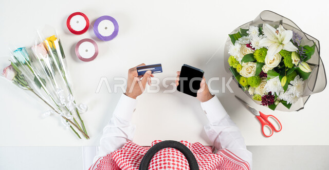الحصول على أدوات الزهور عبر الإنترنت، صناعة وبيع وشراء باقات الورد عبر الإنترنت، صورة ليدي رجل سعودي خليجي يستخدم الهاتف المحمول للدفع من خلال بطاقة الصراف البنكية، استخدام التكنولوجيا في التعلم والتدريب من خلال المواقع الإلكترونية، عرض شاشة سوداء فارغة، خلفية بيضاء