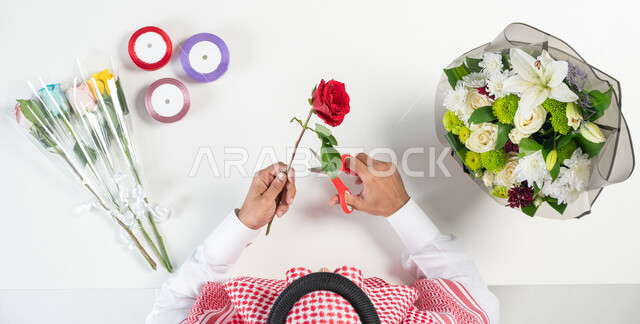 Learn how to prepare and prepare a flower bouquet, make gifts to express love, a portrait of a Saudi Arabian Gulf man using rose pruning scissors, next to him a group of colorful flowers, a white background