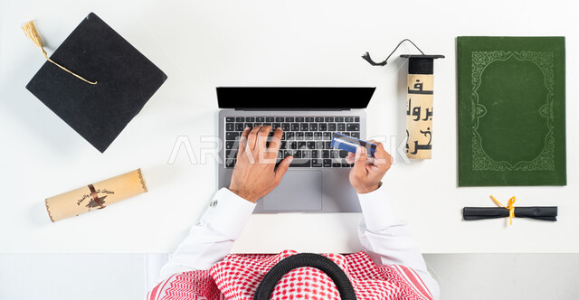 استخدام تطبيقات التسوق عن بعد، الاستفادة من التكنولوجيا الحديثة لطلب مستلزمات التخرج عن طريق الأونلاين، بورتريه ليدي رجل عربي خليجي سعودي يقوم باستخدام الحاسوب المحمول للدفع عن طريق بطاقة الصراف البنكية، البيع والشراء عبر الانترنت، عرض شاشة سوداء فارغة، خلفية بيضاء