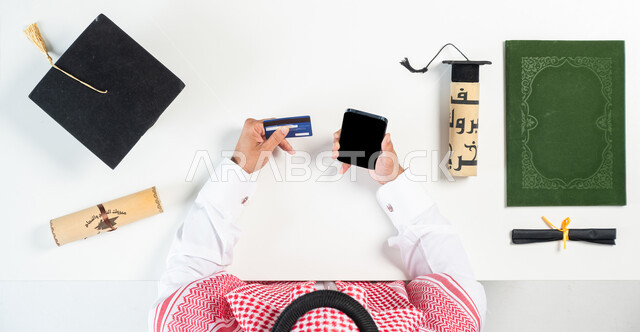 Using remote shopping applications, taking advantage of modern technology to order graduation supplies online, buying and selling online, a portrait of a Saudi Gulf Arab man using a mobile phone to pay by bank ATM card, displaying a blank black screen, a white background