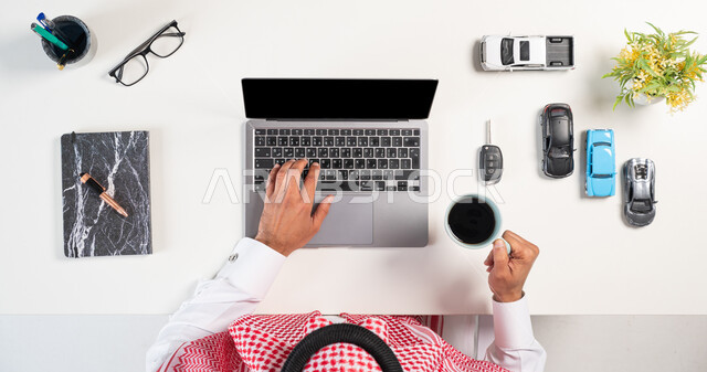 مفهوم التسوق عبر المواقع الالكترونية، استعمال التقنيات في طلب المستلزمات، الحصول على السيارات الحديثة اونلاين، بورتريه علوي عامودي لرجل عربي خليجي سعودي يرتدي الثوب التقليدي والشماغ يستخدم الحاسوب بجانبه مجموعة سيارات وكتاب يشرب فنجان من القهوة، خلفية بيضاء