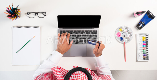 الاهتمام بالنشاطات والهوايات، ممارسة موهبة الرسم والتلوين، الدفع عبر بطاقة الصراف البنكية، بورتريه علوي عامودي لرجل عربي  خليجي سعودي يرتدي الثوب التقليدي يقوم باستخدام الحاسوب، الحصول على دفتر الرسم والألوان المائية أونلاين، عرض شاشة سوداء فارغة، خلفية بيضاء