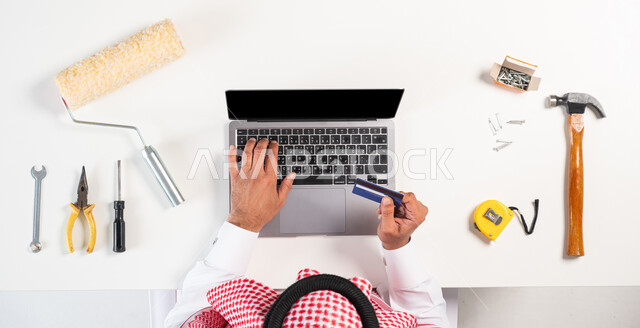 طلب العمال والمهندسين من خلال المواقع الإلكترونية، الحصول على أدوات الصيانة والدهان عبر الإنترنت، الدفع عبر بطاقة الصراف البنكية، بورتريه علوي عامودي  لرجل عربي خليجي سعودي يرتدي التقليدي والشماغ يقوم باستخدام الحاسوب، عرض شاشة سوداء فارغة، خلفية بيضاء