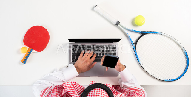 Online shopping and purchasing, ordering products via mobile phone applications, a portrait of a Saudi Gulf Arab man wearing the traditional Saudi dress, using the mobile phone, obtaining sports and entertainment equipment online, displaying a blank black background, a white background