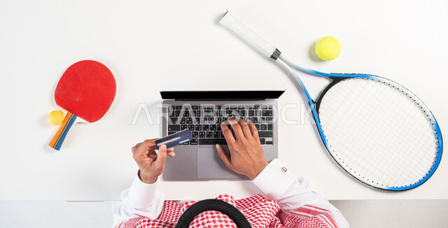 التسوق والشراء أونلاين، طلب المنتجات عبر تطبيقات الحاسوب، دفع الفواتير عبر المواقع الالكترونية الحديثة، بورتريه لرجل عربي خليجي سعودي يرتدي الثوب السعودي التقليدي يقوم باستخدام الحاسوب، الحصول على الأدوات الرياضية والترفيهية عبر الإنترنت، عرض خلفية سوداء فارغة، خلفية بيضاء