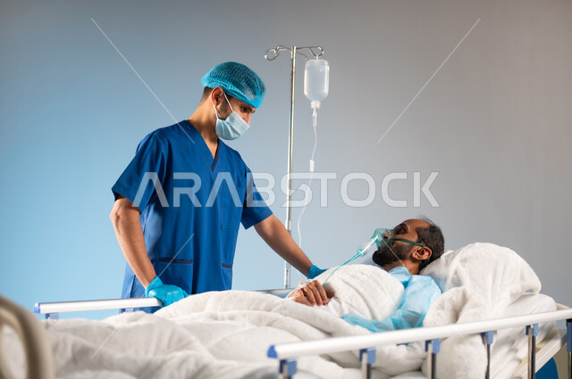 اتباع الإجراءات الاحترازية من فايروس كورونا، مفهوم العناية الطبية، النظرات التي يملؤها التفاؤل والأمل والابتسامة، تلقي العلاج والرعاية الصحية،  بورتريه مقرب لرجل عربي خليجي سعودي مستلقي على السرير يرتدي يونيفورم العمليات يضع كمامة الأكسجين, خلفية زرقاء