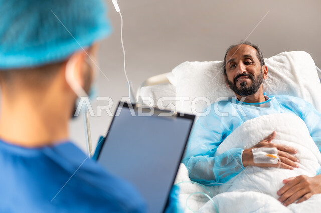 إجراء الفحوصات والمتابعة الدورية للمرضى, الابتسامة والنظر والانتباه الى الممرض لسماع التعليمات الطبية، خدمات العناية الطبية في المستشفيات السعودية, صورة ضبابية مقربة لرجل عربي خليجي سعودي مستلقي على السرير يرتدي يونيفورم العمليات, خلفية زرقاء