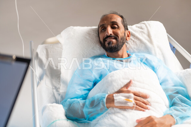 الابتسامة والنظر والانتباه الى الممرض لسماع التعليمات الطبية، خدمات العناية الطبية في المستشفيات السعودية, صورة ضبابية مقربة لرجل عربي خليجي سعودي مستلقي على السرير يرتدي يونيفورم العمليات, إجراء الفحوصات والمتابعة الدورية للمرضى, خلفية زرقاء