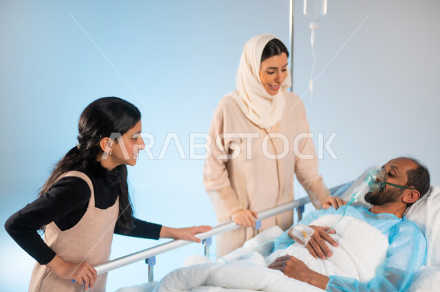 شعور الشخص المصاب بالإرهاق والتعب وأهمية العناية به، الاهتمام والإعتناء بالمريض ورعايته، بورتريه مقرب لرجل عربي خليجي سعودي يرتدي يونيفورم العمليات مستلقي على السرير يضع كمامة الأكسجين بجانبه زوجته وابنته مبتسمين, ايماءات العطف والحنان، خلفية زرقاء