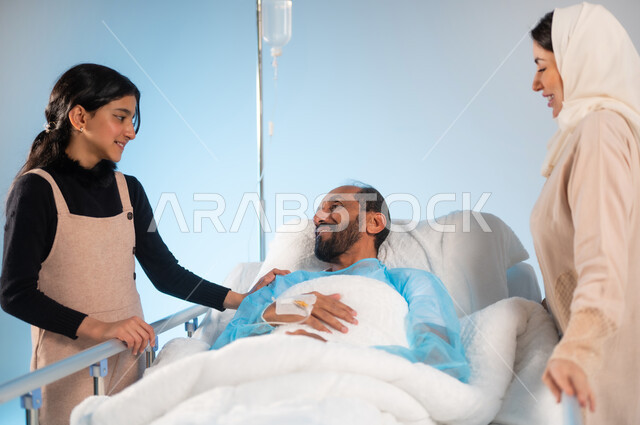 نظرات مليئة بالعطف والحنان والاهتمام، تلقي العلاج والعناية في المستشفى، مفهوم الطب والرعاية الصحية، بورتريه مقرب لرجل عربي خليجي سعودي يرتدي يونيفورم العمليات مستلقي على السرير يقفون بجانبه زوجته وابنته وعلى وجههم ابتسامة, خلفية زرقاء