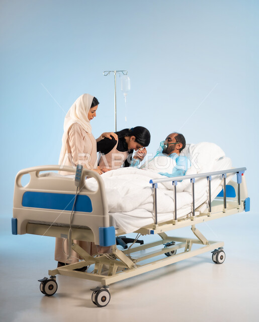 Gestures of sadness and sympathy, concern and care for the patient and his care, the feeling of exhaustion and fatigue of the person with fatigue and the importance of taking care of him, a portrait of a Saudi Gulf Arab man wearing an operating uniform lying on the bed with an oxygen mask next to him, his wife and daughter kissing his hand, blue background
