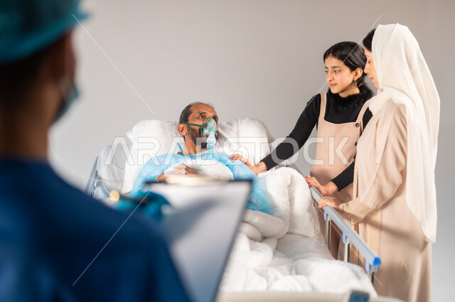 تلقي العلاج والعناية في المستشفى, الاهتمام بالمرضى والتشخيص العلاجي لهم, تدوين المعلومات والملاحظات الطبية, صورة ضبابية مقربة لرجل مريض عربي خليجي سعودي يرتدي يونيفورم العمليات مستلقي على السرير بجانبه عائلته, مفهوم الطب والرعاية الصحية، خلفية زرقاء