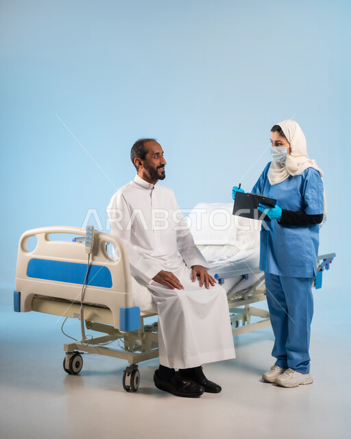 تلقي العلاج وتقديم الخدمات للمرضى, مفهوم الطب والرعاية الصحية، بورتريه لممرضة عربية خليجية سعودية ترتدي بونيفورم العمل والكمامة تقوم بتدوين معلومات المريض، الوقاية من فايروس كورونا، العمل في المراكز الطبية والمستشفيات السعودية، صورة الجسم بالكامل, خلفية زرقاء
