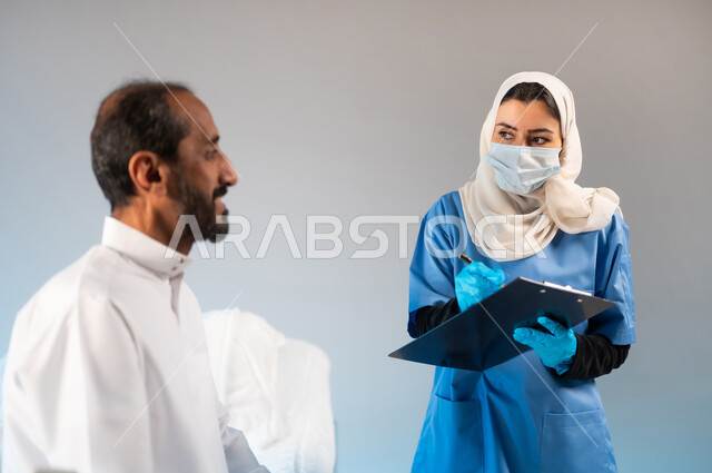 محاولة تجنب انتشار العدوى الفيروسية, التشخيص العلاجي الطبي في مستشفيات المملكة, بورتريه مقرب لممرضة عربية خليجية سعودية ترتدي الكمامة ويونيفورم العمل تقوم بتدوين معلومات المريض, اتباع اجراءات الوقاية الاحترازية من فايروس كورونا, خلفية رمادية
