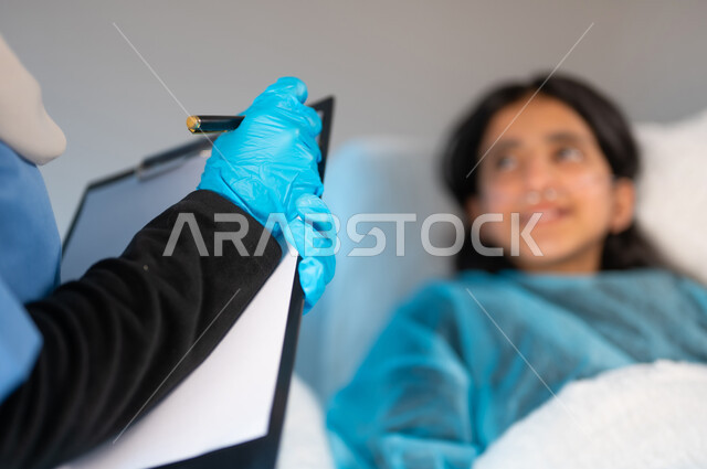 الاهتمام بالمرضى والتشخيص العلاجي لهم, تدوين المعلومات والملاحظات الطبية, بورتريه مقرب ضبابي لفتاة مريضة عريبة خليجية سعودية ترتدي يونيفورم العمليات تستلقي على السرير, تلقي العلاج والعناية في المستشفى الخاص بالأطفال, خلفية رمادية