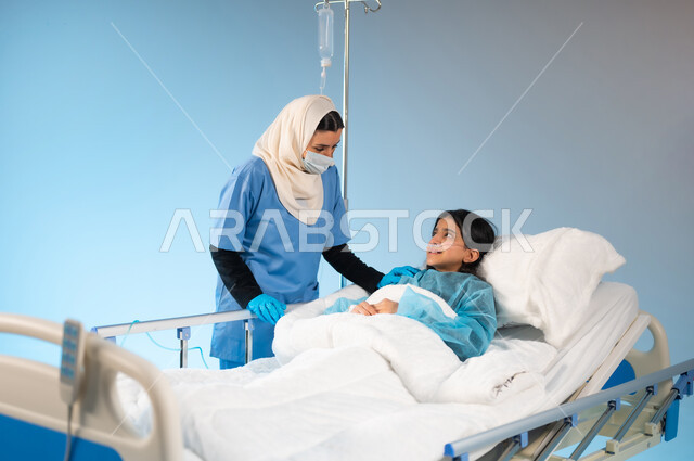أهمية القيام بالفحوصات الدورية للأولاد, مفهوم الطب والرعاية الصحية, اتباع اجراءات الوقاية من فايروس كورونا, تقديم الدعم النفسي للمرضى, بورتريه لممرضة عربية خليجية سعودية ترتدي يونيفورم العمل والكمامة تقف بجانب الفتاة المريضة, خلفية زرقاء