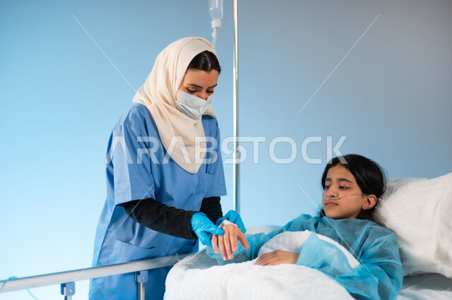 مهن ووظائف نسائية, مفهوم العناية والاهتمام بالمرضى, بورتريه لممرضة عربية خليجية سعودية تقوم بفتح الشريان الوريدي لفتاة مريضة ترتدي يونيفورم العمليات مستلقية على السرير, شعور الشخص المريض بتعب وألم وإرهاق, تقديم الرعاية الصحية في المستشفى, خلفية زرقاء