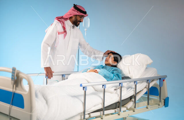 تلقي العلاج والعناية في المستشفى, نظرات مليئة بالعطف والحنان والاهتمام, مفهوم العناية الطبية والخوف على صحة الأبناء, بورتريه لرجل عربي خليجي سعودي يرتدي الثوب التقليدي والشماغ يقف بجانب ابنته المستلقية على السرير, خلفية زرقاء