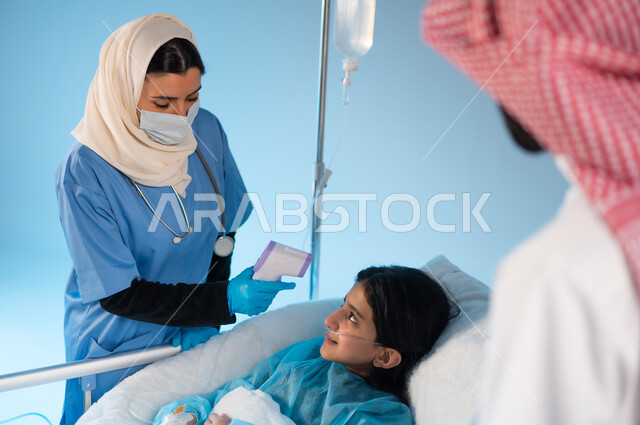 Caring for and taking care of children, the feeling of a person suffering from fatigue and the importance of taking care of him, a portrait of a Saudi Arabian Gulf nurse wearing a work uniform, checking the patient’s temperature using a digital device, following precautionary prevention measures against the Corona virus, a blue background