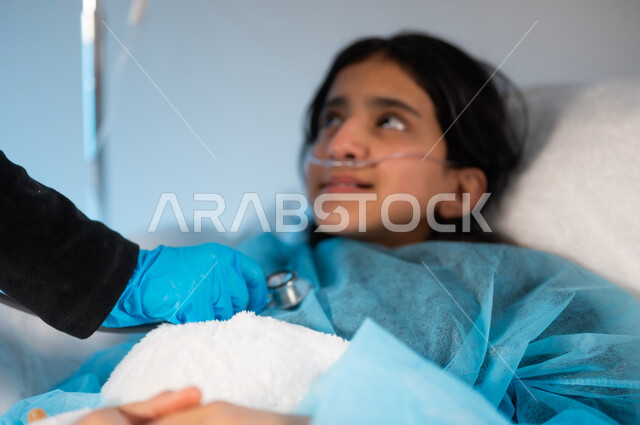 إجراء الفحوصات والتحضيرات للعملية الجراحية, بورتريه مقرب لفتاة عربية خليجية سعودية ترتدي يونيفورم العمليات مستلقية على السرير, مستشفى خاص للأطفال في المملكة, تلقي العلاج والعناية بالصحة للأطفال, خلفية زرقاء