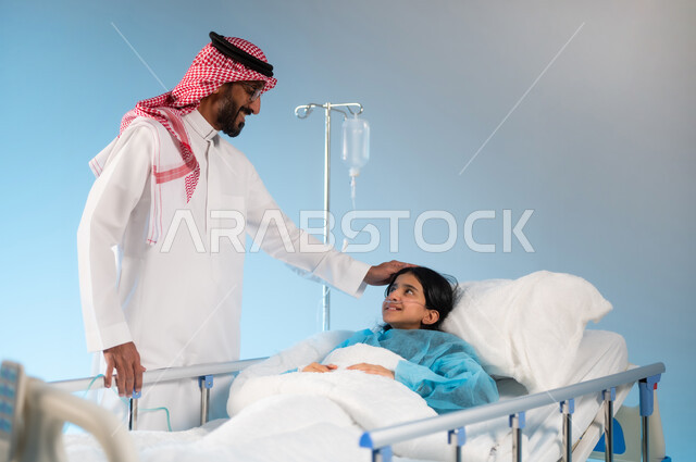 تلقي العلاج والعناية في المستشفى, مفهوم العناية الطبية والخوف على صحة الأبناء, بورتريه لرجل عربي خليجي سعودي يرتدي الثوب التقليدي والشماغ يقف بجانب ابنته المستلقية على السرير, خلفية زرقاء
