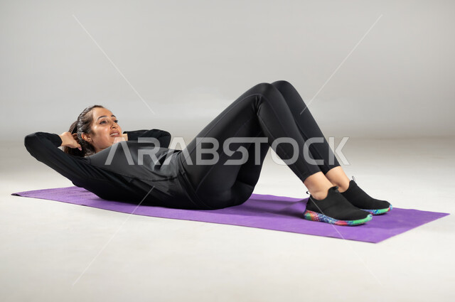 تخصيص أوقات للأنشطة البدنية , بورتريه لامرأة عربية خليجية سعودية ترتدي ملابس رياضية , تقوية العضلات و حرق الدهون , شد و نحت الجسم بممارسة التمرينات الرياضية , أسلوب حياة صحي , صورة للجسم بالكامل , خلفية رمادية