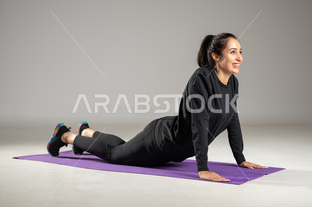 تمارين حرق الدهون و إنقاص الوزن , بورتريه لامرأة عربية خليجية سعودية ترتدي ملابس رياضية , المحافظة على رشاقة الجسم  , تعابير النشاط و الحيوية , ممارسة الأنشطة الرياضية , صورة للجسم بالكامل ,خلفية رمادية