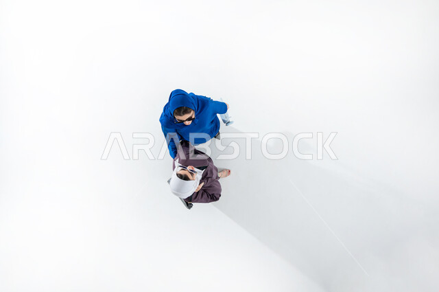 مواكبة تصاميم الأزياء والموديلات الحديثة, بورتريه عامودي علوي لشابتان عربيتان خليجيتان محجبتان ترتديان العباءات الملونه العصريه والنظارات الشمسيه تحملان حقائب شخصيه ملونه بايماءات الأنوثة واللطافة, التسويق للمنتجات السعودية والماركات العالمية الفاخرة, خلفيه بيضاء