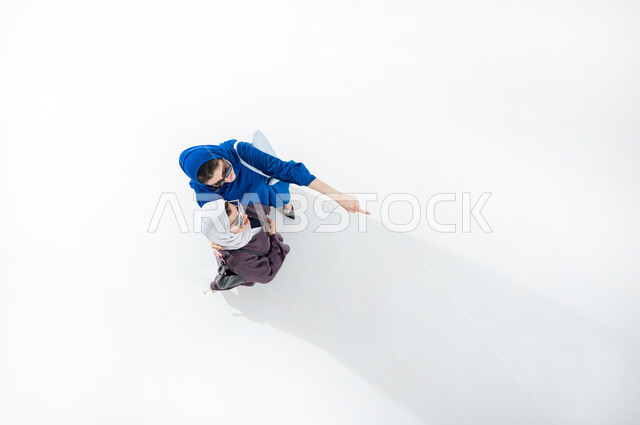 قضاء أوقات ممتعة مع الأصدقاء، بورتريه عامودي علوي لصديقتان عربيتان خليجيتان سعوديتان محجبتان  ترتديان العباءه العصرية الملونه والنظارات الشمسية تشيران بايماءات الفرح والسرور، الاشاره الى شئ ما، أحدث الأزياء النسائية المعاصرة، مفهوم الموضة والأناقة، خلفية بيضاء