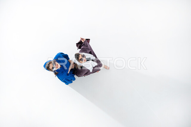 متعة الخروج مع الأصدقاء، ايماءات اللطافة والظرافة، بورتريه عامودي علوي لسيدتان عربيتان خليجيتان سعوديتان محجبتان ترتديان عباءات عصريه ملونه والنظاره الشمسيه تحملان بيدهما شنطهما الشخصيه، قضاء الوقت مع الاخوات في الخارج، ايماءات السعاده والسرور، خلفيه بيضاء