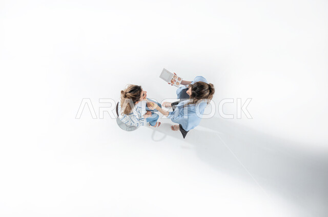 Concept of beauty and skin care, makeup tools tutorial, vertical upper portrait of a smiling Saudi Arabian Gulf hairdresser wearing casual summer clothes applying makeup to a client, preparing for parties and events, holding weddings and performing wedding parties, white background