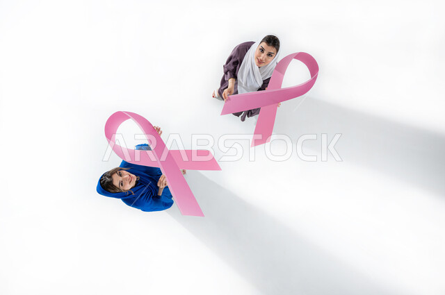اليوم العالمي للتوعية والكشف المبكر عن سرطان الثدي, تحدي الأمراض الخبيثة, بورتريه عامودي علوي لامراتان عربيتان خليجيتان سعوديتان محجبتان ترتديان العباءه الملونه، الامساك بشعار الحملة العالمية، خلفيه بيضاء