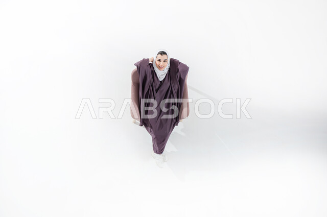 الاستمتاع بوقت الراحة والهدوء , أخذ قسط من الاسترخاء و التأمل, بورتريه عامودي علوي لشابة عربية سعودية خليجيه مبتسمه تجلس على كرسي مريح  تضم يديها خلف راسها, إيماءات وتعابير وجه ويدين تدل على الاسترخاء، الشعور بالسعاده والاستجمام, خلفية بيضاء