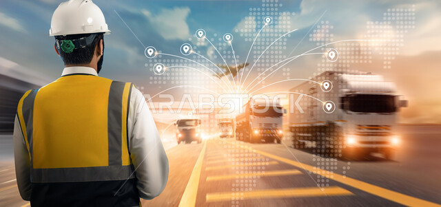 الاستيراد والتصدير حول العالم، الاشراف على شحن الحاويات التجاريه والكونتينرات، مفهوم النقل البري عبر الشاحنات، مهندس عربي خليجي سعودي يرتدي السترة وخوذة الحماية يقوم بتتبع عملية وصول البضائع عبر الاجهزة التقنية