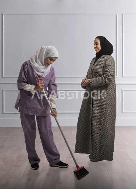 خادمة افريقية تستخدم المكنسة اليدوية، استقدام العمالة الخارجية المرخصة والمؤهلة، المعامله الحسنه للخادمات، توفير خدمات العناية بالمنزل والنظافة والترتيب، سيدة عربية خليجية سعودية ترتدي الحجاب والعباءة تقوم بشكر العامله المنزليه على النظافه والإهتمام