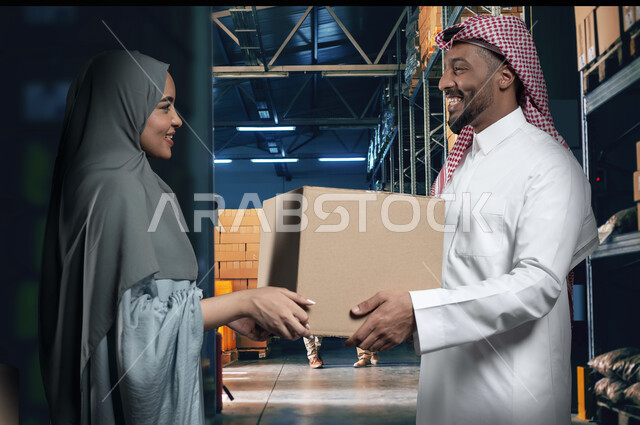 إيماءات الفرح والسرور لامتلاك منزل، مفهوم الانتقال الى سكن جديد، التشارك والتعاون ضمن الأسر السعودية، صورة مقربة لزوجين عربيين خليجيين سعوديين يتعاونان في ترتيب وتنظيم الأغراض المنزلية، صناديق وحاويات كرتونية