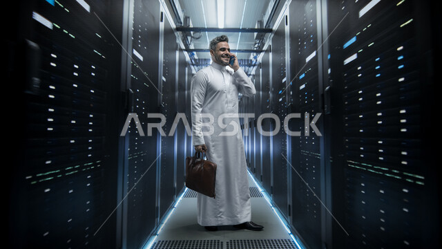 Server control room and internet servers, data storage network, Saudi Arabian Gulf businessman wearing traditional thobe holding a leather bag making a call on a mobile phone standing in data center, server and data storage yard, digital development and future technology