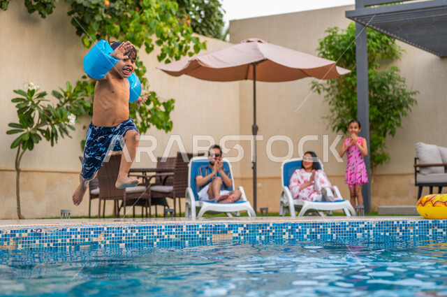 القفز في المسبح مليء بالماء، الأجواء الصيفية الممتعة، الاستمتاع بقضاء عطلة صيفية سعيدة، رحلة سياحية ترفيهية، ولد عربي خليجي سعودي يرتدي عوامة السباحة ويقفز في بركة مائية