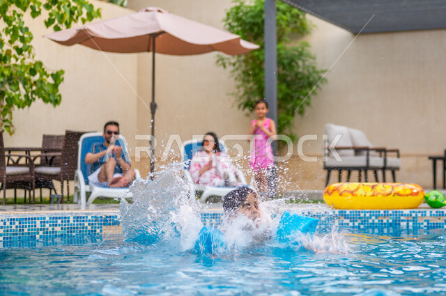 استعمال عوامة السباحة للقفز في المسبح، الأجواء الصيفية الممتعة، الاستمتاع بقضاء عطلة صيفية سعيدة، رحلة سياحية ترفيهية، ولد عربي خليجي سعودي يقفز في بركة مائية