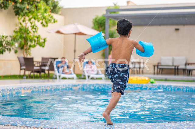 الاستمتاع بالأجواء الصيفية الممتعة، قضاء عطلة صيفية سعيدة، ارتداء عوامة السباحة للقفز في المسبح، رحلة سياحية ترفيهية، ولد عربي خليجي سعودي يقفز في بركة مائية