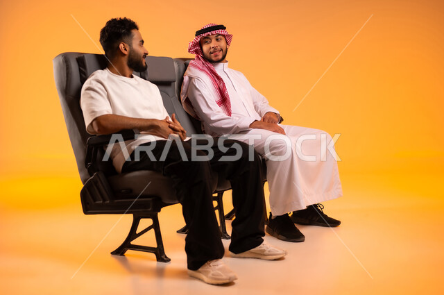Sitting in the airport lounge, social relations between friends, socializing and getting to know each other, chats and dialogues between friends, a portrait of a Saudi Gulf Arab man wearing the traditional dress and shemagh sitting with his friend spending enjoyable times, the importance of tourism in Saudi Arabia, orange background