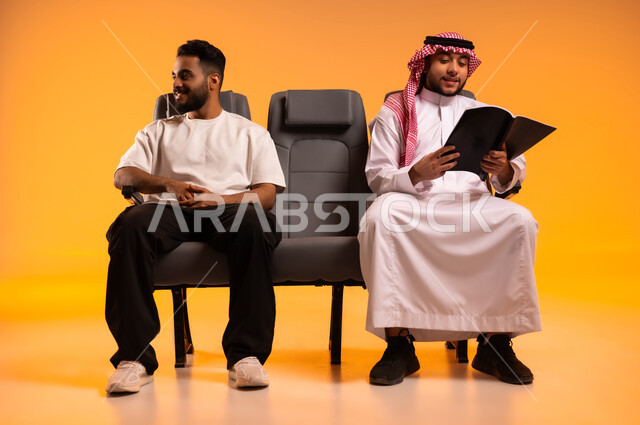 شغف التعرف على الكتب المحتلفة، قضاء وقت الفراغ بالتعلم والتثقف الذاتي، الاستعداد للسفر في إجازة، الجلوس في صالة المطار, بورتريه لرجل عربي خليجي سعودي يرتدي الثوب التقليدي والشماغ يجلس على المقعد مع صديقه، أهمية السياحة في السعودية, خلفية برتقالية