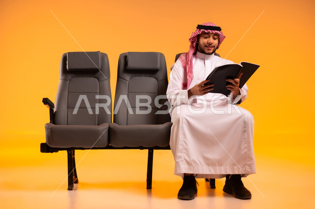 شغف التعرف على الكتب المحتلفة، قضاء وقت الفراغ بالتعلم والتثقف الذاتي، الاستعداد للسفر في إجازة، الجلوس في صالة المطار, بورتريه لرجل عربي خليجي سعودي يرتدي الثوب التقليدي والشماغ يجلس على المقعد يمسك بيده كتاب, أهمية السياحة في السعودية, خلفية برتقالية