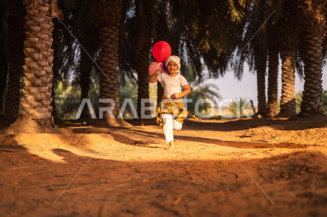 قضاء الوقت واللعب في الهواء الطلق، طفل عربي خليجي سعودي مبتسم يرتدي زي الحصاد والعمامة يقوم بالركض وحمل مجموعة بوالين ملونة داخل مزارع النخيل المثمرة، ايماءات البهجة والفرح، الحفاظ على تراث زراعي غني، مهن تقليدية سعودية