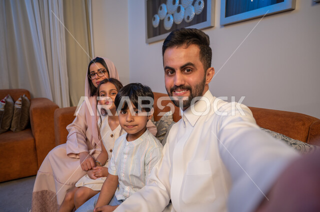 توثيق اللحظات السعيدة، النظر الى الكاميرا بسعادة وسرور، أجواء عائلية مليئة بالحب والمودة، أب عربي خليجي سعودي يرتدي الثوب التقليدي يلتقط صورة سيلفي برفقة زوجته وابنائه، التقاط صور تذكارية