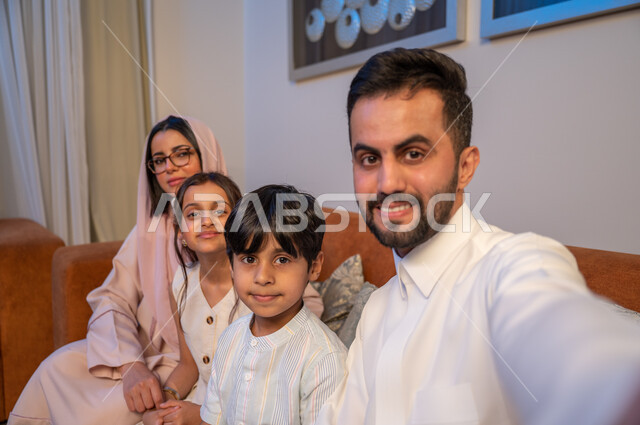 التقاط صور تذكارية، توثيق اللحظات السعيدة، النظر الى الكاميرا بسعادة وسرور، أجواء عائلية مليئة بالحب والمودة، أب عربي خليجي سعودي يرتدي الثوب التقليدي يلتقط صورة سيلفي برفقة زوجته وابنائه