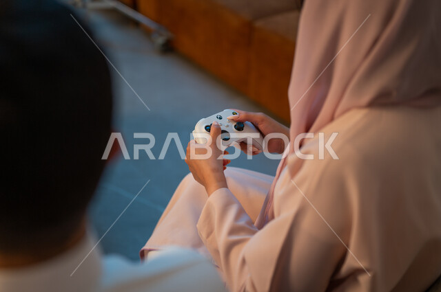 تقنيات الكترونية حديثة ترفيهيه, قضاء وقت ممتع ومسلي في المنزل، التفاعل والاندماج مع ألعاب الفيديو، زوجان عربيان خليجيان سعوديان يمسكان عصا التحكم بتعابير السرور والسعادة، فعاليات عطلة نهاية الأسبوع