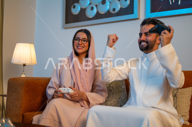 Gestures of enthusiasm and engagement with video games, spending a fun and entertaining time at home, a Saudi Gulf Arab couple holding the joystick with expressions of pleasure and happiness, weekend activities, modern electronic entertainment technologies
