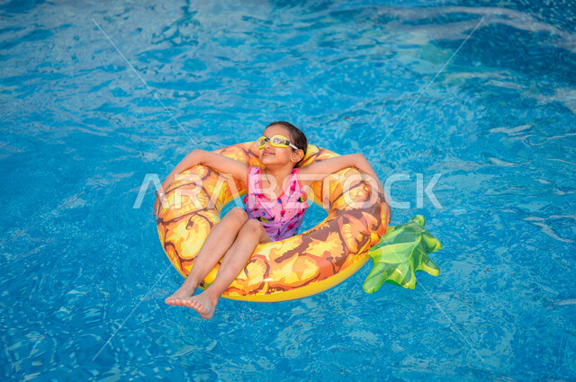 أنشطة ترفيهية مسلية في العطلة, إيماءات السعادة و الاستمتاع بالفعاليات الصيفية, قضاء أوقات ممتعة في المسبح, فتاة عربية خليجية سعودي ترتدي ملابس السباحة تجلس داخل عوامة السباحة في بركة المياه، منتجعات شاطئية في السعودية